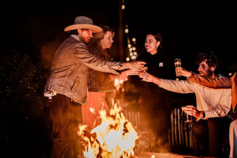 Un gruppo di amici brinda accanto al fuoco di notte nella Safari tent Cozy di TinyParks Cast Away, Paesi Bassi.