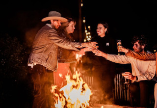Un gruppo di amici brinda accanto al fuoco di notte nella Safari tent Cozy di TinyParks Cast Away, Paesi Bassi.