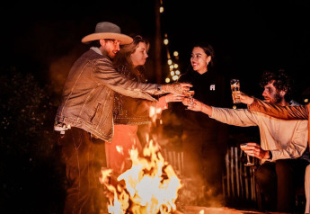 Vriendengroep rond kampvuur bij nacht in Safari tent Cozy van TinyParks Cast Away, Nederland, met drankjes.