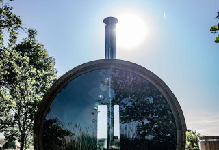 Ronde houten sauna met spiegelglas, zon en bomen bij TinyParks Cast Away, Nederland.