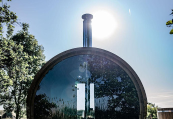 Round wooden sauna with reflective glass, sunlight and trees, at TinyParks Cast Away, Netherlands.