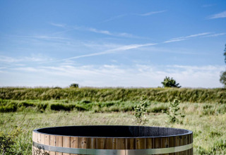 Houten hot tub buiten bij Safari tent Cozy op TinyParks Cast Away, Nederland, met blauwe lucht erboven.