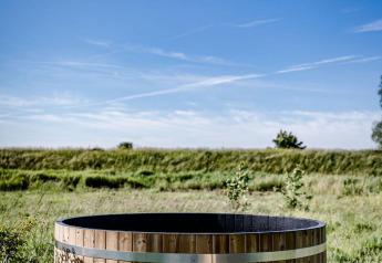 Houten hot tub buiten bij Safari tent Cozy op TinyParks Cast Away, Nederland, met blauwe lucht erboven.
