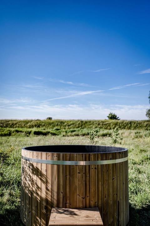 Outdoor wooden hot tub by Safari tent Cozy at TinyParks Cast Away, Netherlands, beneath a clear blue sky.