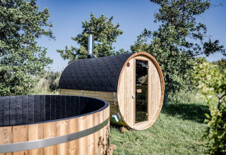 Outdoor view of a barrel sauna and a hot tub at Safari tent Cozy, TinyParks Cast Away, Netherlands.