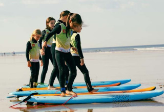 Kinder lernen am Strand nahe Les Sables-d'Olonne das Surfen, stehen auf Brettern im Sand und tragen Neoprenanzüge.