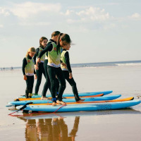 Børn lærer at surfe på stranden nær Les Sables-d'Olonne, iført dragter og stående på surfbrætter.