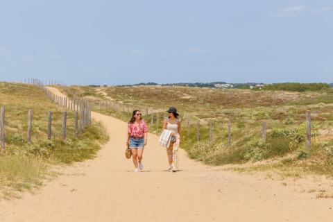 Dos mujeres caminan por un sendero arenoso en Camping Le Bois de la Gachère en Pays de la Loire, Francia.