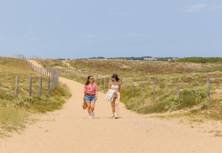 Zwei Frauen spazieren auf einem sandigen Weg bei Camping Le Bois de la Gachère im Pays de la Loire, Frankreich.