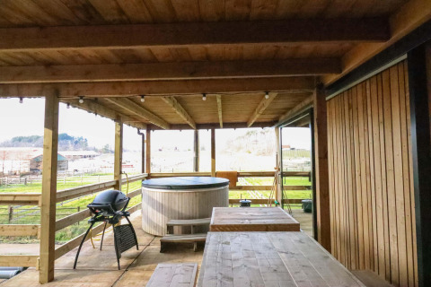 Terraza de madera con jacuzzi, parrilla y mesa en el tiny house Cosy Cabins en el bosque de Limburg, Bélgica.