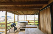 Terraza de madera con jacuzzi, parrilla y mesa en el tiny house Cosy Cabins en el bosque de Limburg, Bélgica.