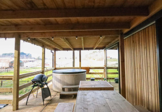 Terraza de madera con jacuzzi, parrilla y mesa en el tiny house Cosy Cabins en el bosque de Limburg, Bélgica.