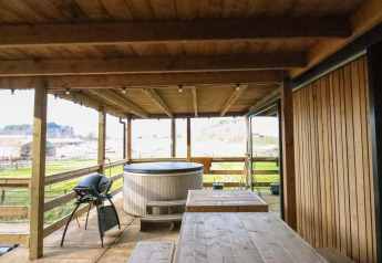 Overdekt terras in hout met jacuzzi, grill en tafel bij Cosy Cabins in het bos van Limburg, België.