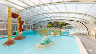 Overdækket børnepool med legedyr og farverige skulpturer på Camping Le Bois de la Gachère, Pays de la Loire.