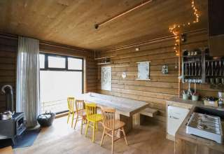 Cocina y comedor con paneles de madera, sillas amarillas, ventana grande y luces acogedoras en la cabaña.