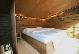Dormitorio acogedor de tiny house con cama doble, paredes de madera y luces cálidas en el bosque de Bélgica.