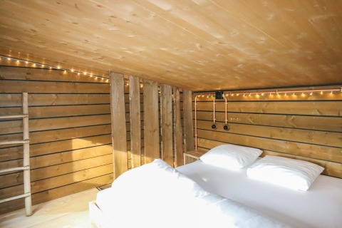 Dormitorio tipo loft con cama doble y paredes de madera en tiny house en el bosque de Limburgo, Bélgica.