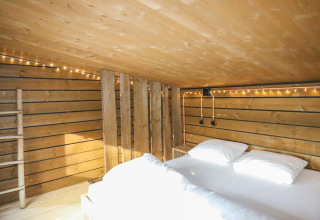 Dormitorio tipo loft con cama doble y paredes de madera en tiny house en el bosque de Limburgo, Bélgica.