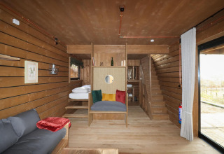 Interior cálido de una minicasa de madera con mobiliario moderno y cojines coloridos en Limburg, Bélgica.