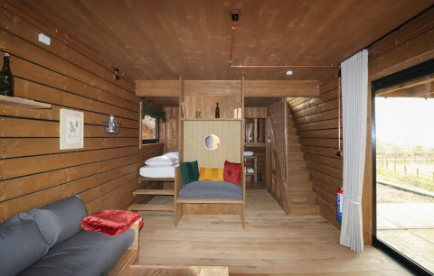 Gezellige houten tiny house met kleurrijke kussens en modern interieur in het bos van Limburg, België.