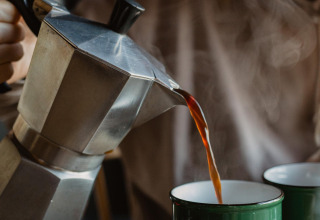 Iemand giet hete koffie uit een moka pot in een groene mok, wat zorgt voor een gezellige sfeer om te ontspannen tijdens het glampen.