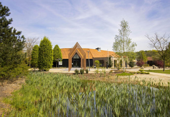 Moderne glampingaccommodatie met unieke driehoekige ingang, omgeven door weelderig groen en een vijver.