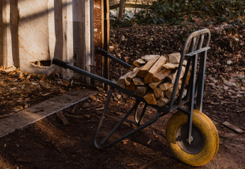 Una carretilla llena de leña apilada junto a una pared rústica en un camping.