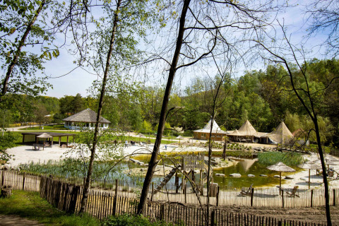 Un sito glamping panoramico con tende, un laghetto e aree per sedersi all'aperto circondate da una lussureggiante foresta verde.