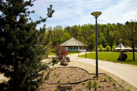 Un site de glamping tranquille avec une cabane ronde, de la verdure luxuriante, des sentiers de promenade et des lampadaires sous un ciel ensoleillé.