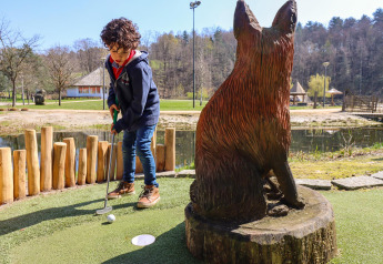 Ragazzo gioca a minigolf presso una sistemazione glamping accanto a una grande scultura di volpe.