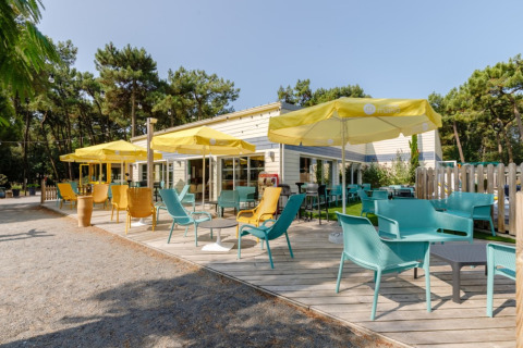 Terraza exterior con sillas coloridas y sombrillas amarillas en Camping Le Bois de la Gachère, Pays de la Loire.