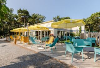 Sonnige Terrasse mit bunten Stühlen und gelben Sonnenschirmen im Camping Le Bois de la Gachère, Pays de la Loire.