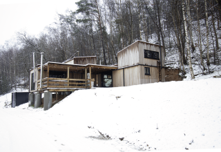 Pequeña casa de madera con jacuzzi en Cosy Cabins, bosque nevado de Limburg, Bélgica, junto a árboles.