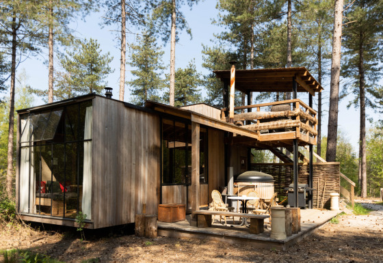 Cabaña moderna de madera Treetrunk con jacuzzi exterior y terraza en la azotea en medio del bosque.