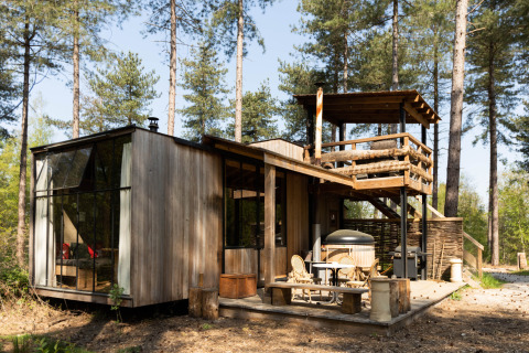 Cabaña moderna de madera Treetrunk con jacuzzi exterior y terraza en la azotea en medio del bosque.