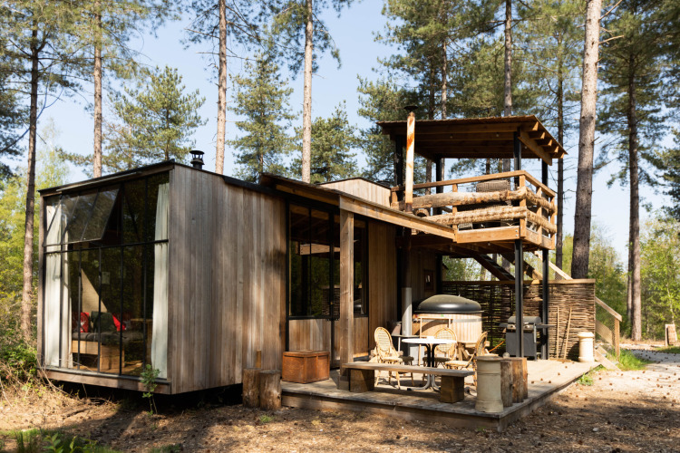 Moderne Holzlodge Treetrunk mit Hot Tub und Dachterrasse, umgeben von hohen Bäumen im Wald.