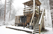 Cabaña de madera cubierta de nieve, con escaleras exteriores y terraza, en el bosque de Limburg, Bélgica.