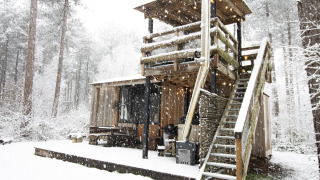 Met sneeuw bedekte blokhut met buitentrap en terras in het bosrijke gebied van Limburg, België.
