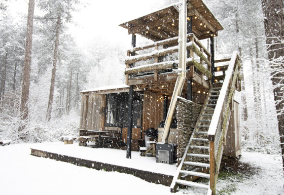 Met sneeuw bedekte blokhut met buitentrap en terras in het bosrijke gebied van Limburg, België.