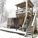 Cabaña de madera cubierta de nieve, con escaleras exteriores y terraza, en el bosque de Limburg, Bélgica.
