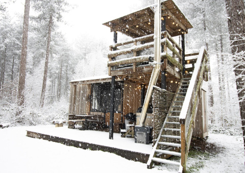 Cabaña de madera cubierta de nieve, con escaleras exteriores y terraza, en el bosque de Limburg, Bélgica.
