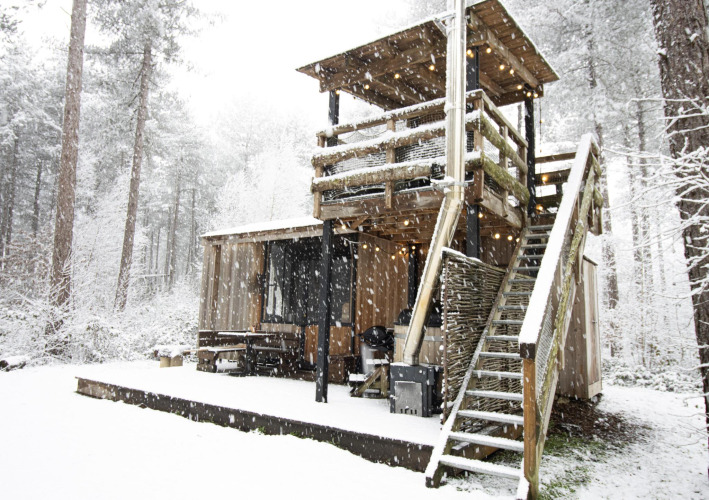 Schneebedeckte Holzhütte mit Außentreppe und Terrasse in einem waldreichen Gebiet Limburgs, Belgien.