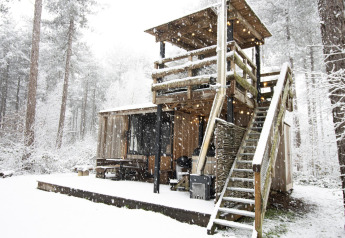 Schneebedeckte Holzhütte mit Außentreppe und Terrasse in einem waldreichen Gebiet Limburgs, Belgien.