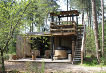 Foto della lodge Treetrunk con vasca idromassaggio esterna, terrazza e piattaforma nel bosco di Limburg, Belgio.