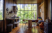 Rustiek glampingverblijf met houten interieur, grote ramen, keuken, eettafel en uitzicht op het bos.