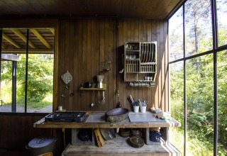 Rustic kitchen area in a lodge with wooden walls, large windows, and a view of the forest outside.