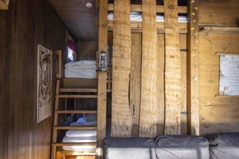 Interior de alojamiento glamping con escalera de madera, literas y cálidos paneles de madera rústica.