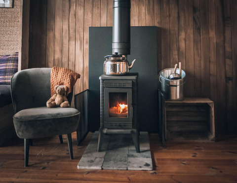 Gemütliche Glamping-Unterkunft mit Holzofen, Sessel samt Teddybär und Eimer in Holzausstattung.