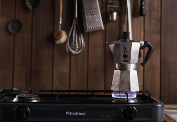 Una moka scalda su un fornello a gas in una cucina da glamping con pareti di legno e utensili appesi.