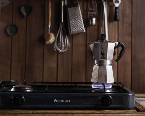 A moka pot heating on a gas stove in a cozy glamping kitchen with wood paneling and hanging utensils.